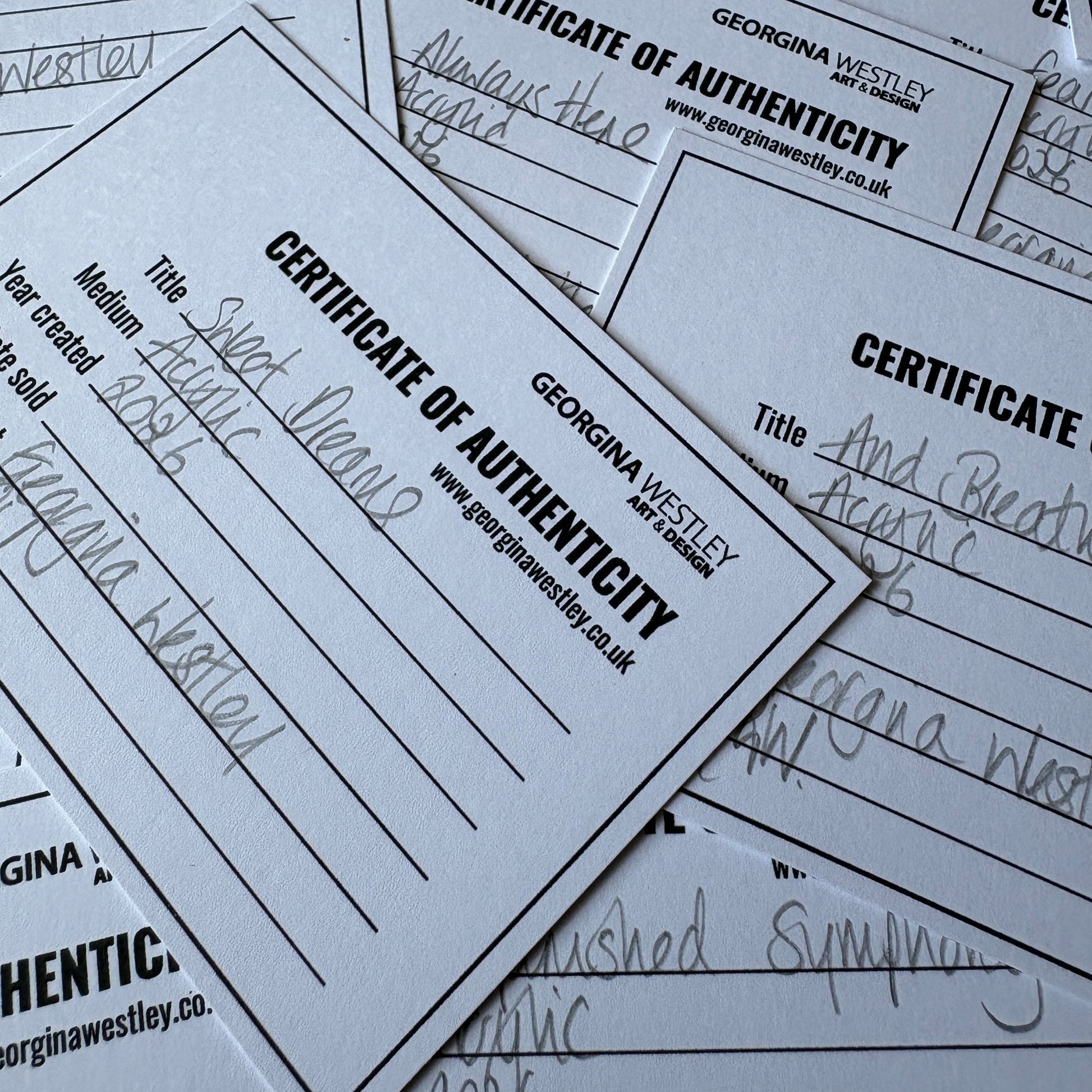 A pile of white paper certificates printed with 'Certificate of Authenticity' and 'Georgina Westley' arranged on top of each other.