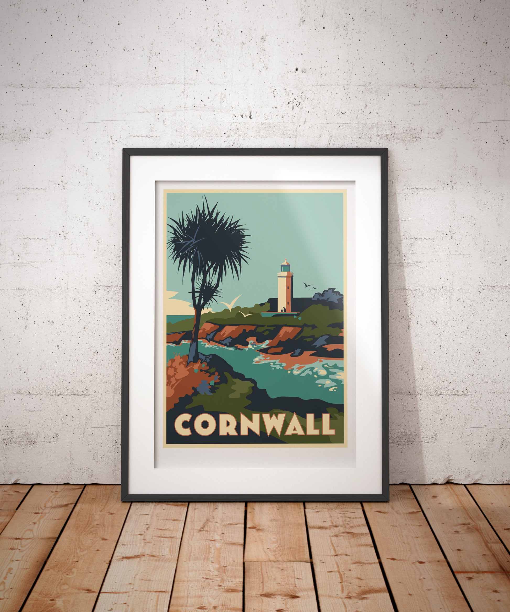 Framed artwork of Cornwall Godrevy Lighthouse by Georgina Westley and coastal scene on a white brick wall.