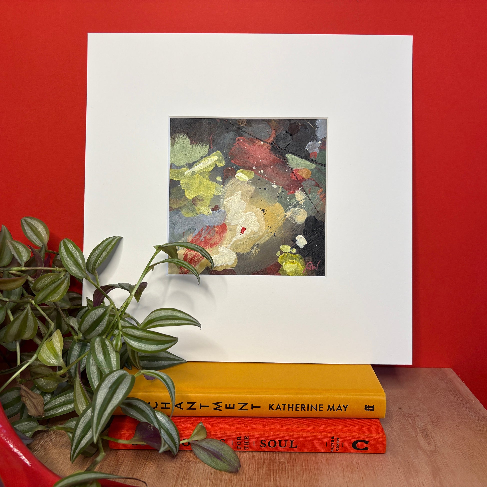 Framed artwork on a table with books and a plant
