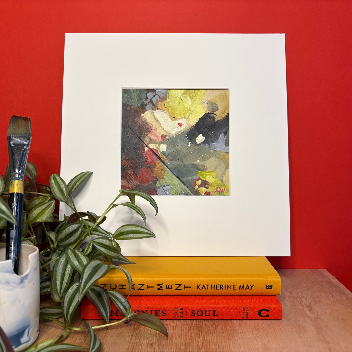 Art on a red wall with books and a plant below