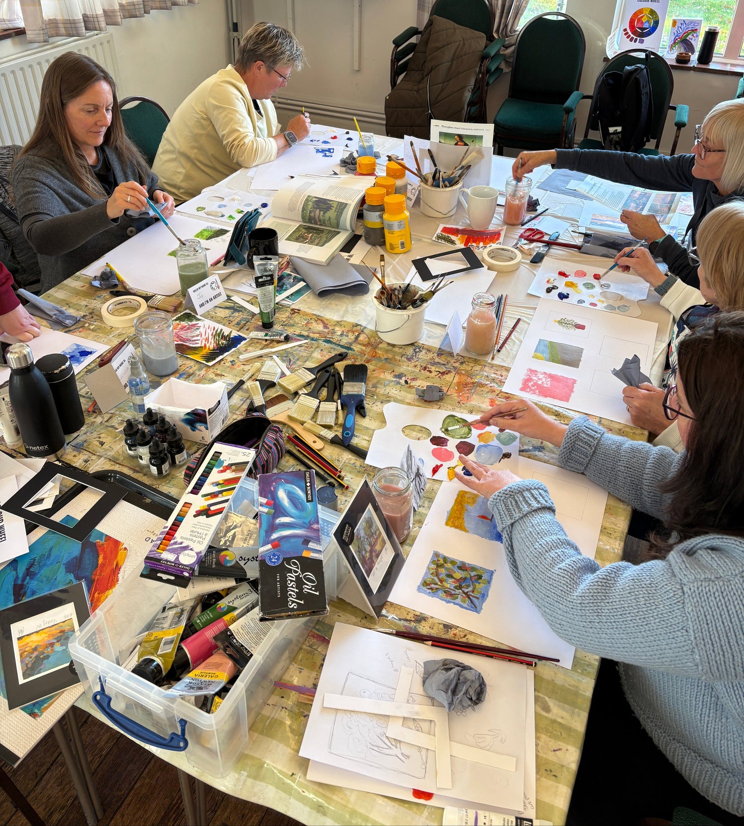 Group of people gathered around a table with art supplies and materials.