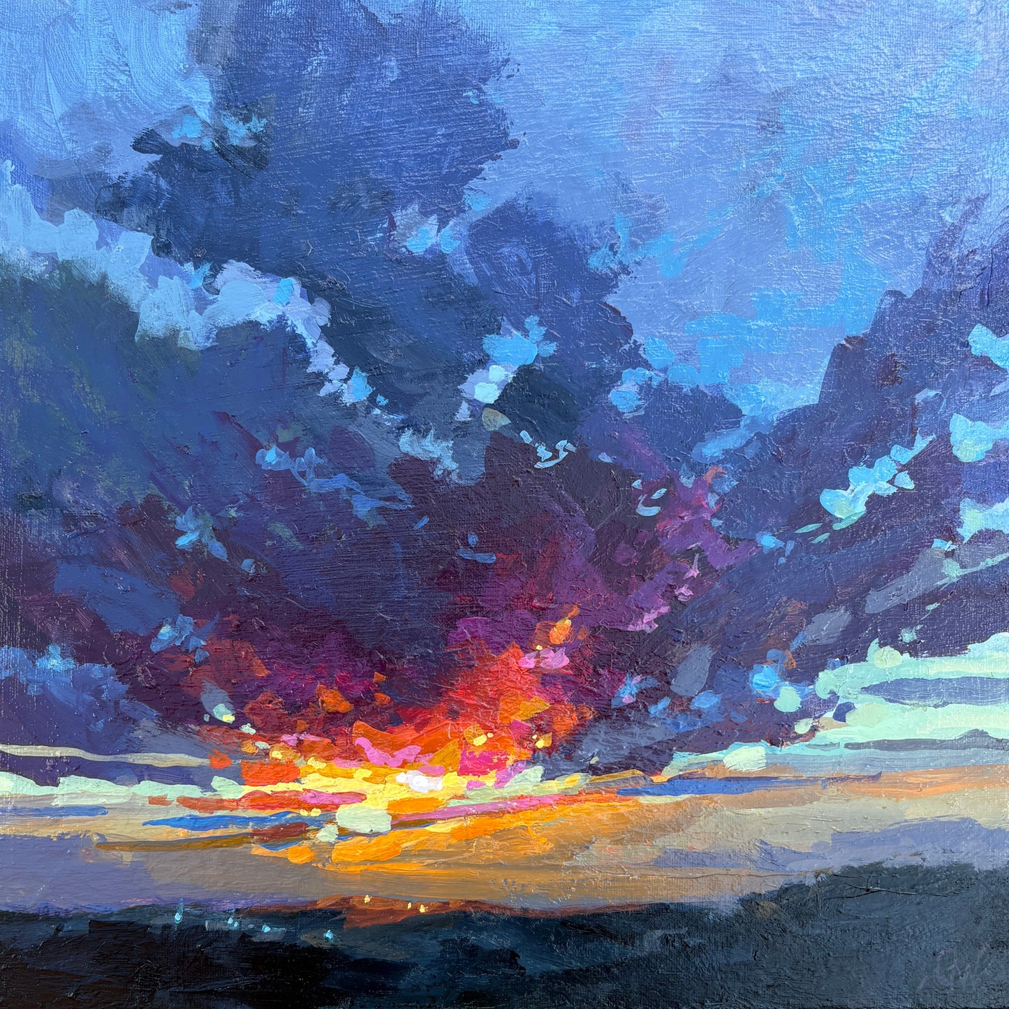 A square framed painting of an abstract sunset scene, featuring dark blue and purple clouds with a bright orange and yellow horizon, set in a light wood frame against a gray stone wall.